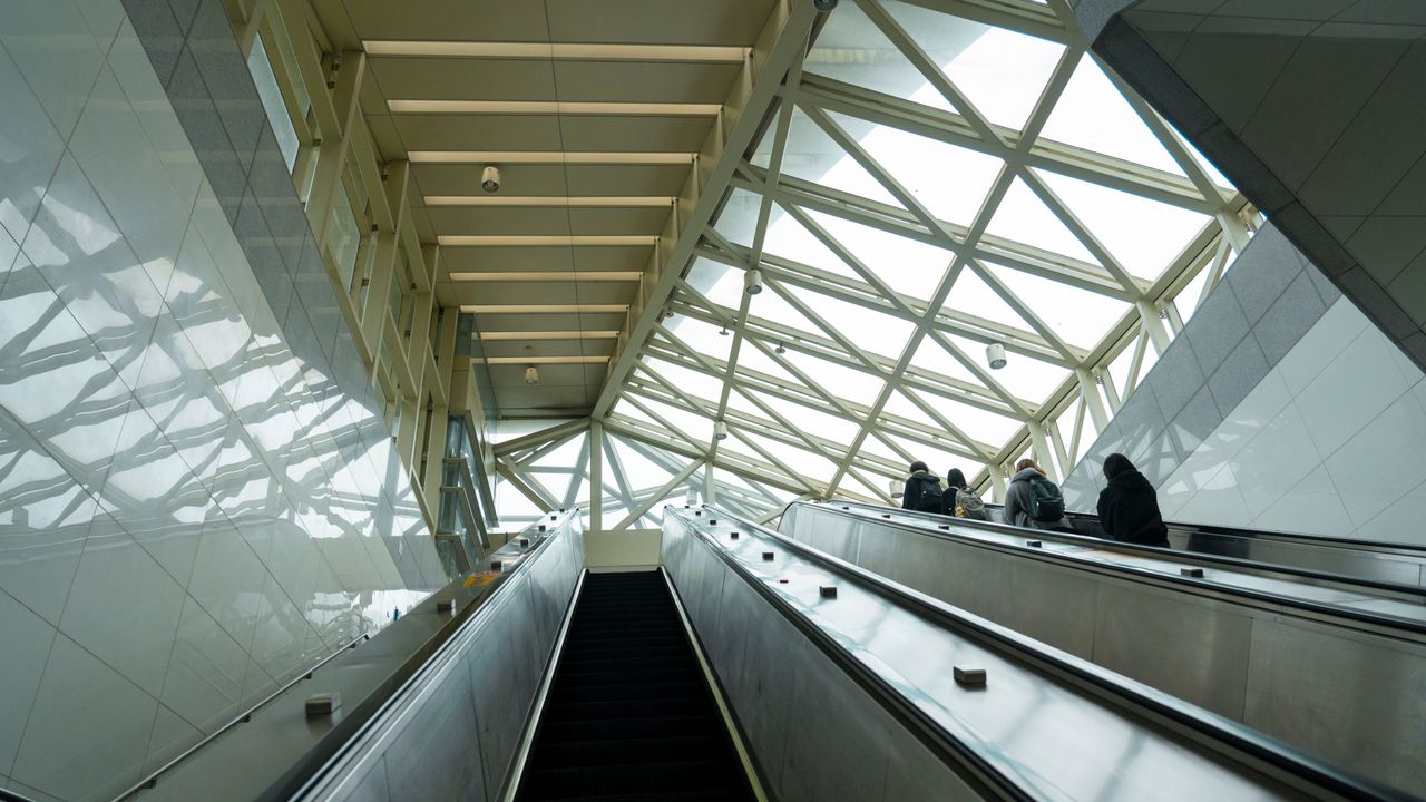 Travellers on escalators beneath a glass and steel terminal roof