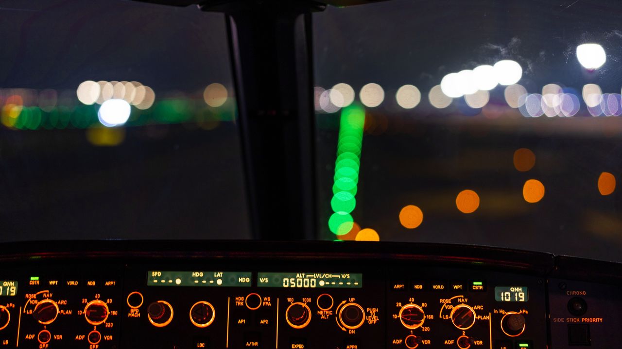 A night view from the flight deck, panel glowing above rows of runway lights