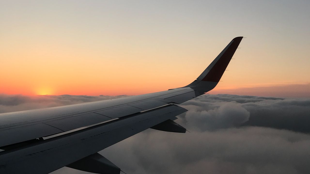 An aircraft wing and winglet above a cloud deck at sunset, seen through a cabin window